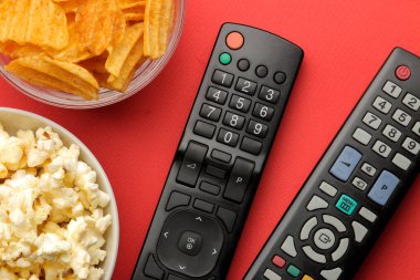 Atıştırmalıklı patlamış mısır ve parlak kırmızı arka planda uzaktan kumanda. Evde film ya da video izleme kavramı. en üstteki görünüm