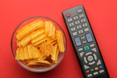 Parlak kırmızı arka planda çipler ve televizyon uzaktan kumandası. Evde film ya da video izleme kavramı. en üstteki görünüm