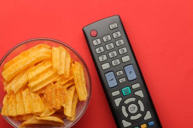 Parlak kırmızı arka planda çipler ve televizyon uzaktan kumandası. Evde film ya da video izleme kavramı. en üstteki görünüm