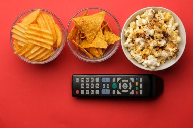 Atıştırmalıklı patlamış mısır ve parlak kırmızı arka planda uzaktan kumanda. Evde film ya da video izleme kavramı. en üstteki görünüm