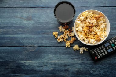 Mavi ahşap bir masada patlamış mısır ve uzaktan kumanda. Evde film ya da video izleme kavramı. en üstteki görünüm