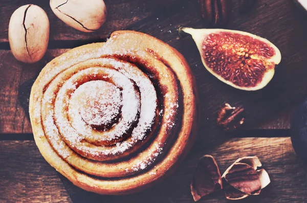 Frisches Zimtbrötchen mit Pekannüssen garniert mit Zuckerpuder auf Holzgrund — Stockfoto