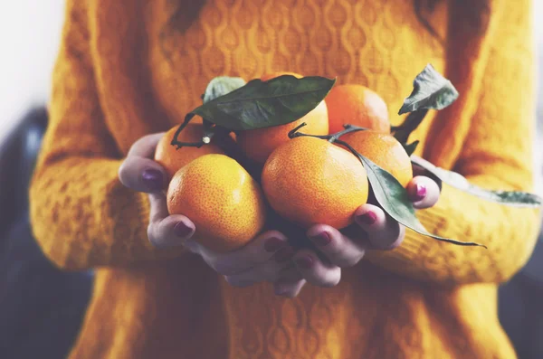 Vrouw in gele gebreide trui met rijpe clementines in haar handen — Stockfoto