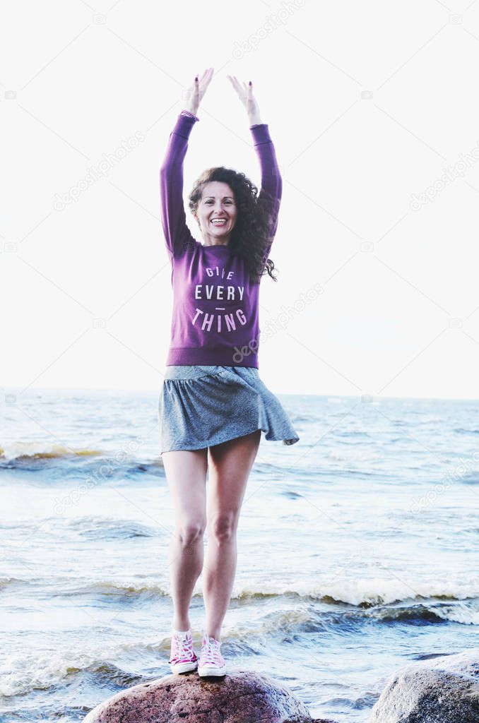 Laughing woman in dress and sweatshirt on the sea beach