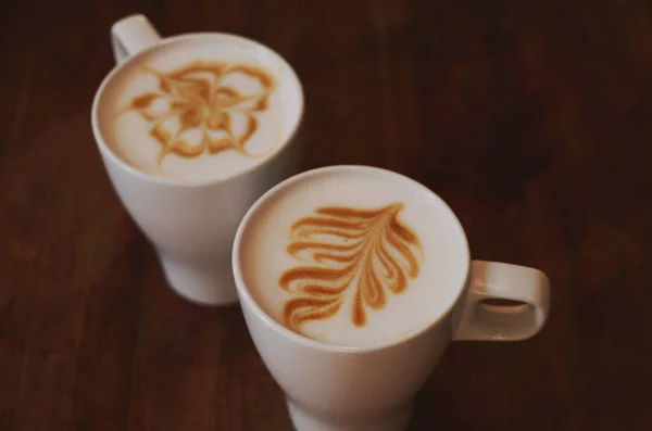 Dva šálky latte na hnědý dřevěný stůl — Stock fotografie