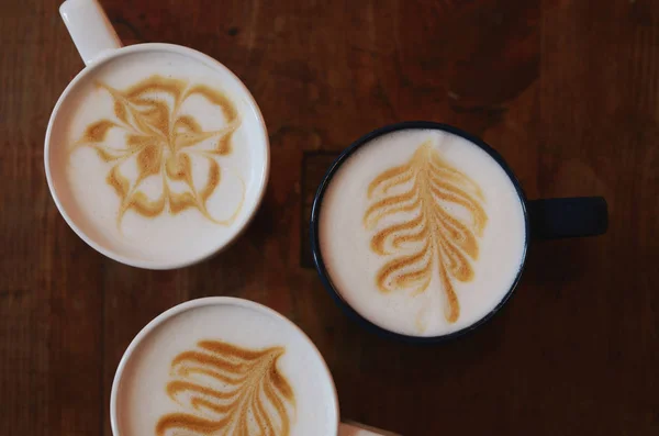 El arte del café con leche - tres tazas sobre el café sobre el fondo oscuro de madera Imágenes de stock libres de derechos
