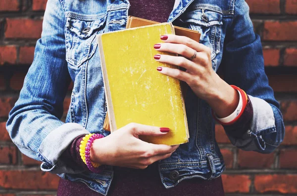 Hipster étudiante fille avec bracelet et ongles rouges tenant pile de livres Image En Vente