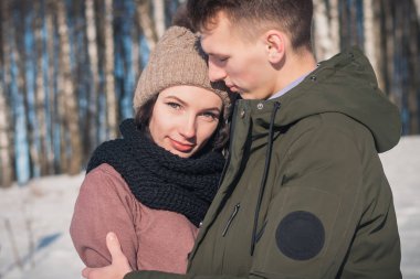 Güneşli bir günde, kış parkında aşık güzel bir çift. Adam kız arkadaşının omzuna sarılıyor.