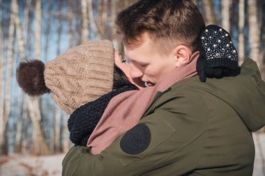Parkta güneşli bir günde genç ve güzel bir çift. Genç adam kız arkadaşına sarılıyor ve onu ısıtıyor.