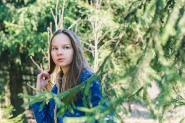 Güneşli bir bahar kozalaklı ormanında uzun saçlı, kot ceketli genç ve zayıf bir kız.