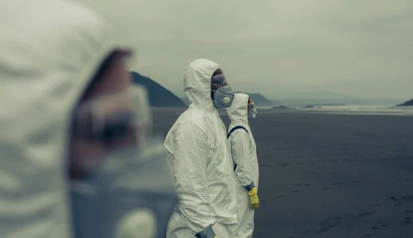 Mensen met bacteriologische beschermingspakken die naar de zee kijken — Stockfoto