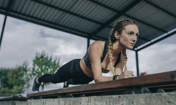 Sportswoman doing plank on a bench — Stock Photo, Image