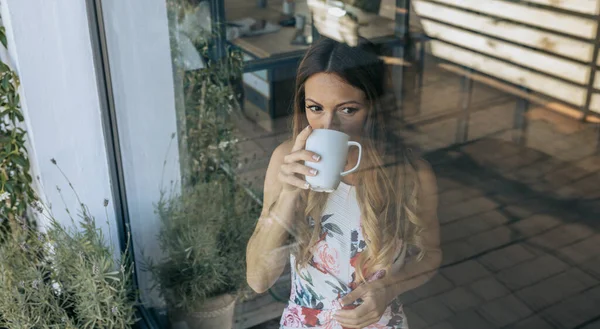 Woman behind the window drinking coffee — Stock Photo, Image