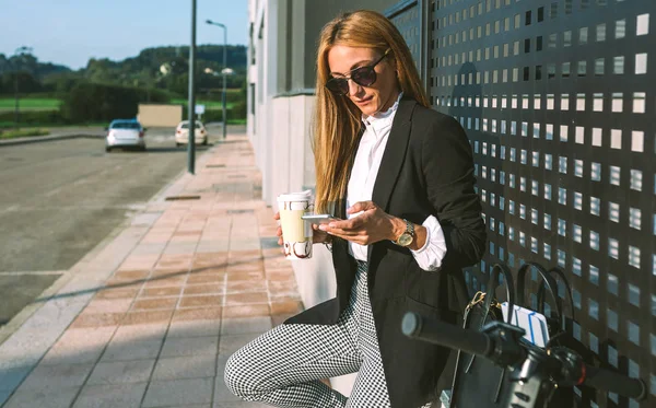 Businesswoman using mobile and drinking coffee with her scooter — Stock Photo, Image