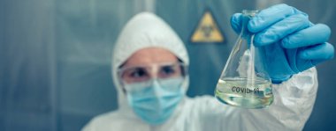 Koruyucu kıyafetli bir bilim adamı laboratuarda test tüpü arıyor.