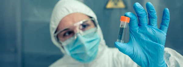 Cientista com terno de proteção olhando frasco no laboratório — Fotografia de Stock