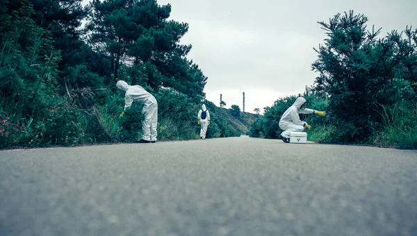 Pessoas em ternos de proteção bacteriológica à procura de amostras em estrada vazia — Fotografia de Stock