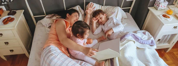 Madre leyendo libro a sus hijos en la cama —  Fotos de Stock
