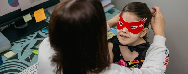 Γυναίκα τηλεργασία και βάζοντας κοστούμι μάσκα στην κόρη της — Φωτογραφία Αρχείου