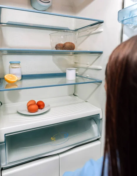 Girl looking at empty fridge due to a crisis — Stock Photo, Image