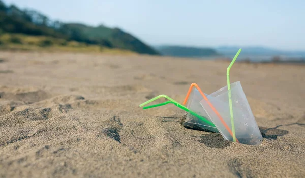 Spiaggia con bicchieri di plastica e cannucce — Foto Stock