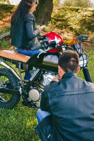 Hombre arreglando su motocicleta mientras su novia mira el móvil — Foto de Stock