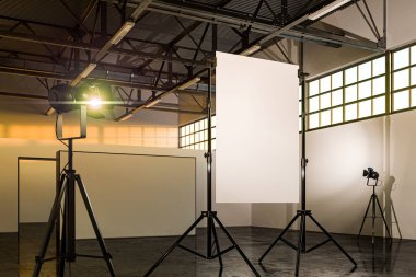 Tripodlar, Modern Parlak Fotoğraf Stüdyosundaki spot ışıklarıyla aydınlatılan, Dikey Boş Beyaz Poster Tutuyorlar. 3B Hazırlama.