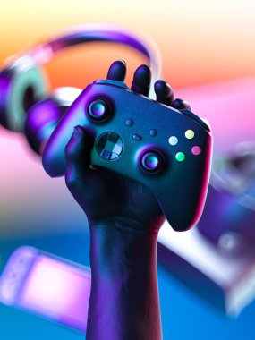 Oyun sahası kontrolörüyle el ele tutuşan kablosuz joystick, VR gözlükleri, kulaklıklar, arka planda video oyun konsolu. 3d oluşturma