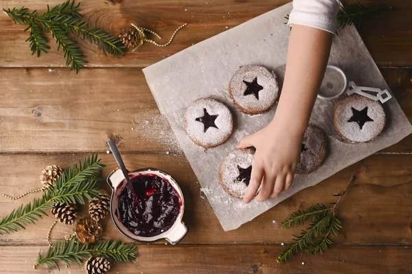 Різдвяне печиво у формі зірки на дерев'яному столі. Бікіні з джемом і порошком, декор з ялинових гілок. Дитяча рука в рамці. Вид зверху. Копіювати простір — стокове фото