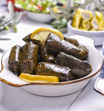 Geleneksel Yunan mutfağı. Üzüm yapraklarına sarılmış pirinç. Limonlu ve baharatlı Dolma. Ev yemeği. Zeytin dalları ve çeşitli baharatlı aperatifler.