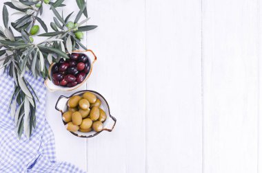 Geleneksel mezeler, Yunan mutfağından yeşil ve kırmızı zeytinler. Beyaz ahşap arka plan. Taze zeytin dalları. Boşluğu kopyala.