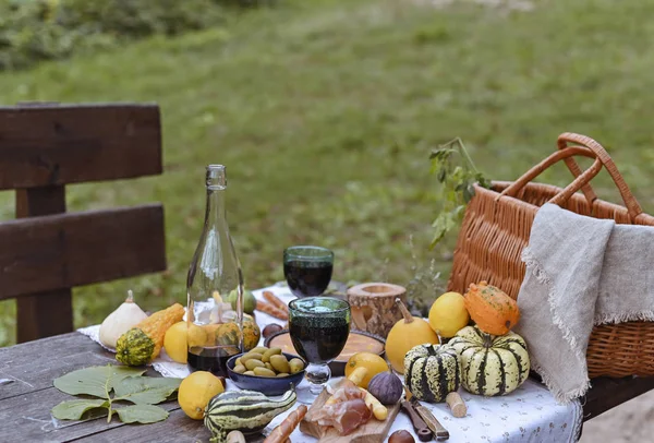 Autumn picnic in the park. Pumpkins, pie, prosciutto and snacks. Bottle of wine and glasses on a wooden table. Sunny day and outdoor recreation.