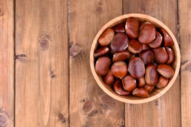 Tahta arka planda bir fincan kestane. Sonbahar hasadı ve olgun meyveler. Metin için boş alan.