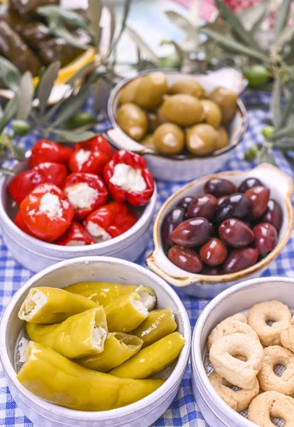 Traditional appetizers, green and red olives from Greek cuisine. Fresh branches of olives. Copy space. Blue checkered tablecloth.