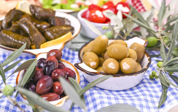 Traditional greek cuisine. Wrapped rice in grape leaves. Dolma with lemon, spices, various pickled olives and hot peppers. Fresh branches and homemade food.