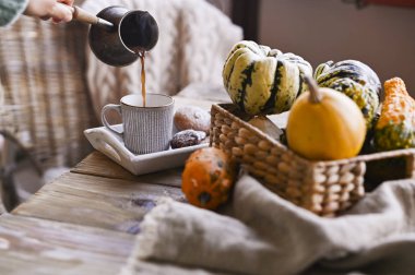 Sonbahar ve kış ev yapımı balkabakları. Örgü kazaklı bir kız taze demlenmiş kahveyi fincana dolduruyor. Ev atmosferi ve dekor kavramı. Tahta masa bisküvisi ve Cinna