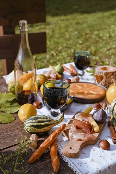 Autumn picnic in the park. Pumpkins, pie, prosciutto and snacks. Bottle of wine and glasses on a wooden table. Sunny day and outdoor recreation.