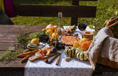 Sonbahar doğasında öğle yemeği için hazırlanmış bir masa, piknik. Hasat, sonbahar yemeği, şarap ve bardaklar. Açık hava toplantısı.
