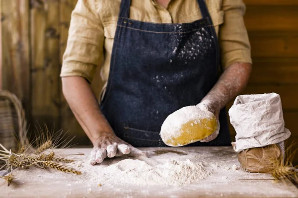 Manos y masa femeninas. Una mujer está preparando una masa para hornear en casa. Foto de estilo rústico. Mesa de madera, espigas de trigo y harina. Espacio libre para texto. —  Fotos de Stock