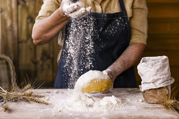 Mãos de mulher, farinha e dongh.Levitation em um quadro de massa e farinha Uma mulher em um avental está preparando massa para assar em casa. Foto de estilo rústico. Mesa de madeira, espigas de trigo e farinha. Foto emocional . — Fotografia de Stock