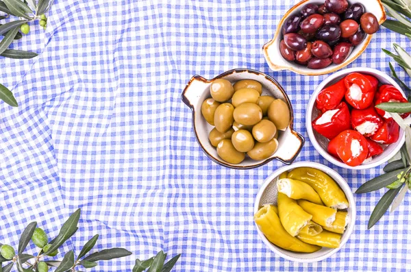 Traditionelle Vorspeisen, grüne und rote Oliven aus der griechischen Küche. Frische Olivenzweige. Kopierraum. Oben. Blau karierte Tischdecke. — Stockfoto