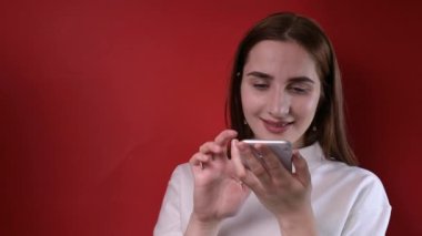 Genç bir kız elinde bir telefon tutuyor. Stüdyoda kırmızı arka planda çekim yapıyoruz. Akıllı telefon iletişimi ve modern teknoloji.