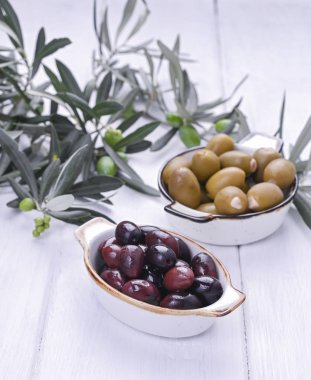 Geleneksel mezeler, Yunan mutfağından yeşil ve kırmızı zeytinler. Beyaz ahşap arka plan. Taze zeytin dalları. Boşluğu kopyala.