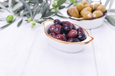 Geleneksel mezeler, Yunan mutfağından yeşil ve kırmızı zeytinler. Beyaz ahşap arka plan. Taze zeytin dalları. Boşluğu kopyala.