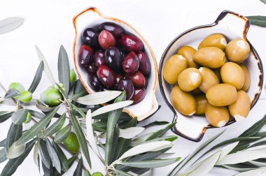 Geleneksel mezeler, Yunan mutfağından yeşil ve kırmızı zeytinler. Beyaz ahşap arka plan. Taze zeytin dalları. Uzayı kopyala Yukarıda.