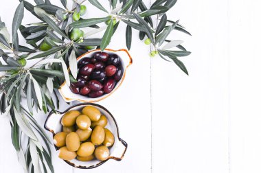 Geleneksel mezeler, Yunan mutfağından yeşil ve kırmızı zeytinler. Beyaz ahşap arka plan. Taze zeytin dalları. Boşluğu kopyala.