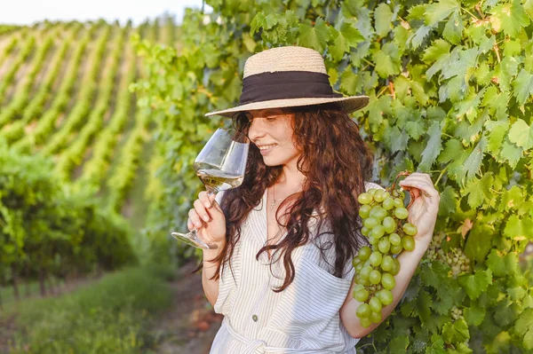 Ragazza con un bicchiere di vino e vigneti. Colline verdi con uva e i raggi del sole al tramonto. Stagione di vendemmia in Italia. — Foto Stock