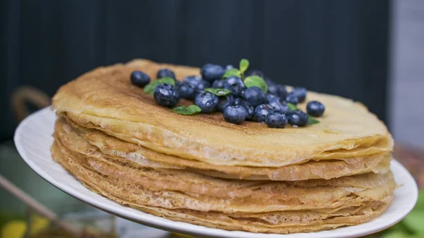 Pancakes with blueberries and honey on a plate, on wooden roofing. Traditional pastries for the Russian festival of Maslenitsa. free space for text. Close-up shot. — Stock Photo, Image