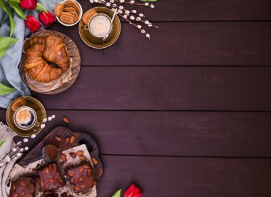 Paskalya kahvaltısında aromatik taze espresso, kruvasan, kek, renkli yumurta, kırmızı lale ve söğüt. Kurabiyeli kahve, ahşap masadaki çiçekler. Yukarıdan görüntüle.