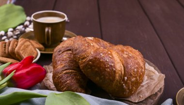Paskalya kahvaltısında aromatik taze espresso, kruvasan, renkli yumurta, kırmızı lale ve söğüt. Kurabiyeli kahve, ahşap masadaki çiçekler. Yukarıdan bak. Boşluğu kopyala.
